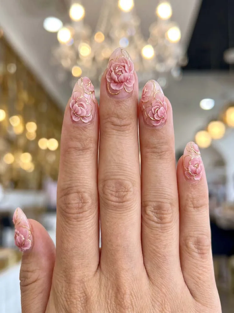 Almond-shaped pink nails with sculpted 3D acrylic peony flowers in blush and rose with fine gold gel pen petal outlines