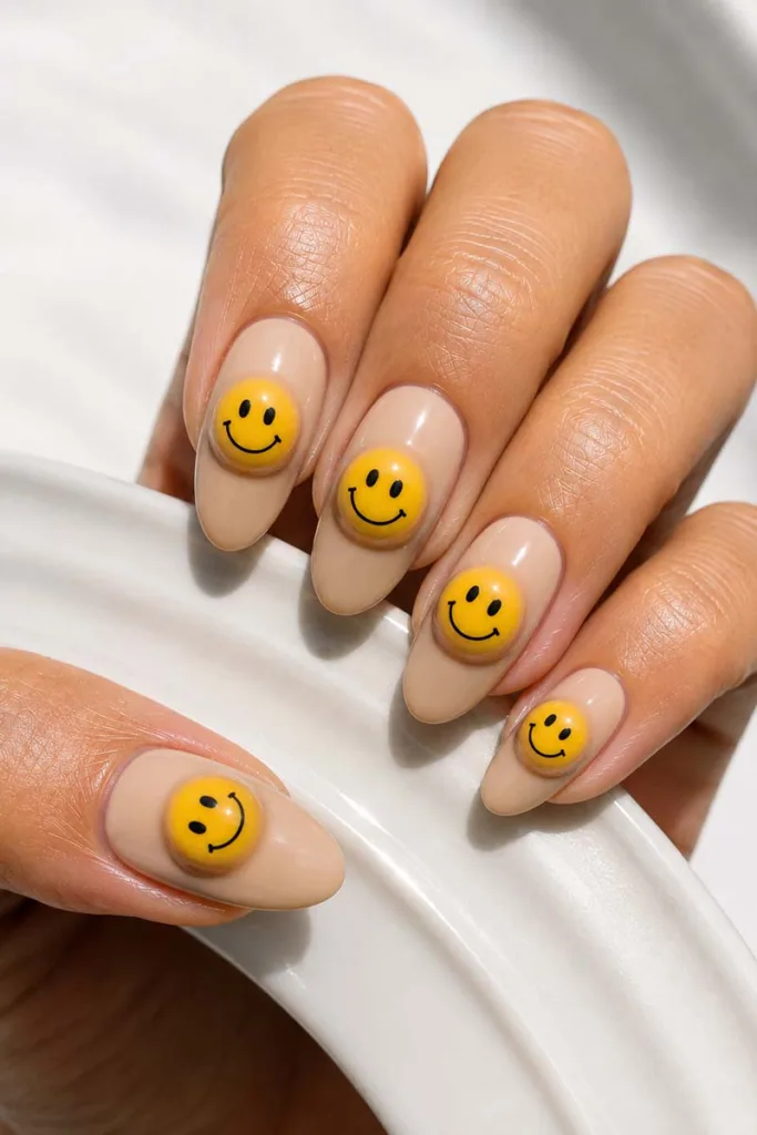Close-up portrait of nude almond-shaped 3D smiley face gel nails with raised dome nail art and glossy finish resting on a white ceramic surface under sharp studio lighting.