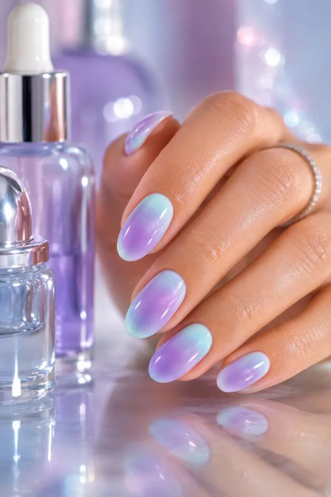 Glossy portrait beauty shot of aqua blue and lavender aura oval nails with soft shimmer beside reflective skincare bottles for summer nail design ideas 2026.