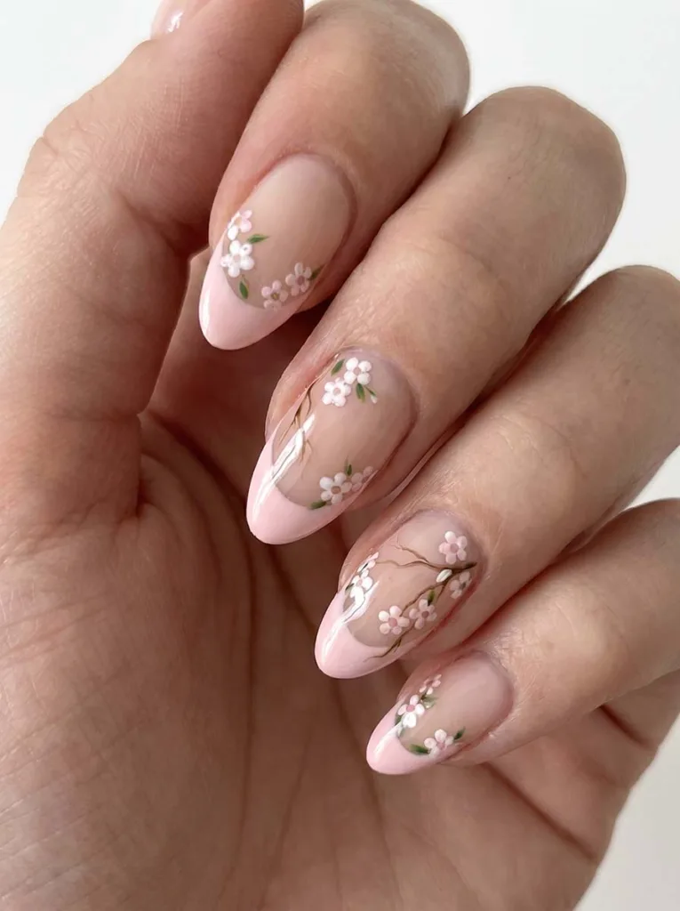 Almond-shaped blush pink floral French tip nails with tiny hand-painted white and pale pink blossom clusters at the smile line
