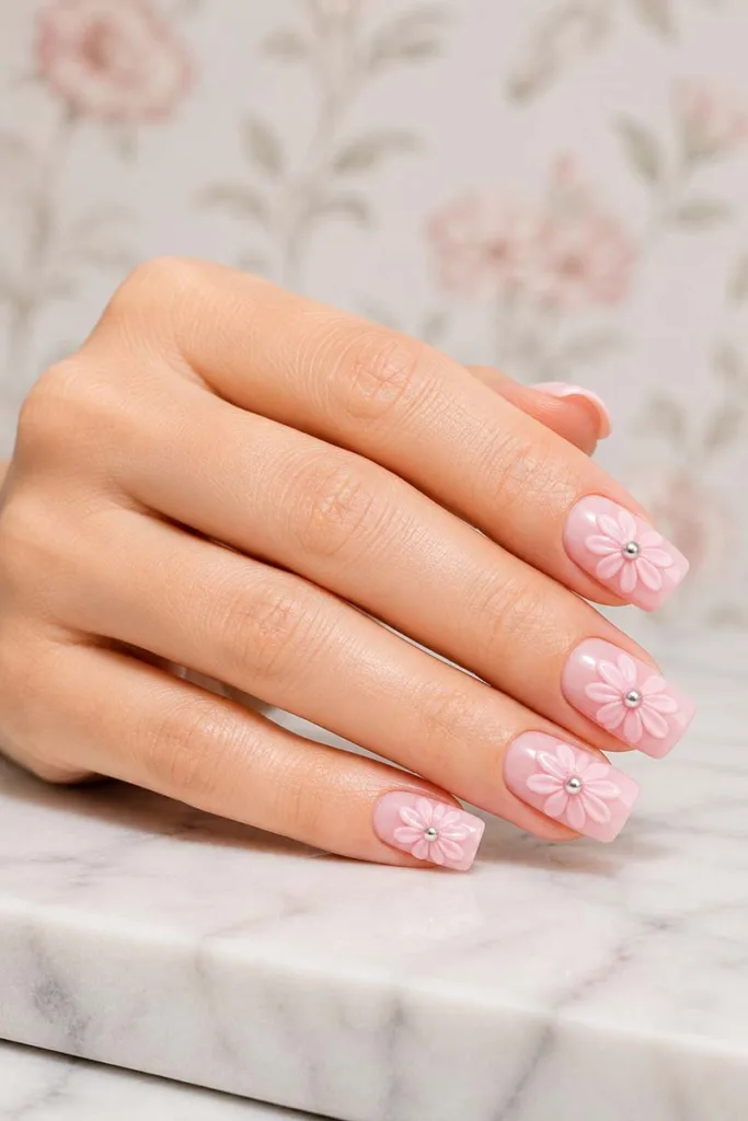 Square pink nails with raised embossed daisy petals and silver caviar bead centers on a soft pink gel base
