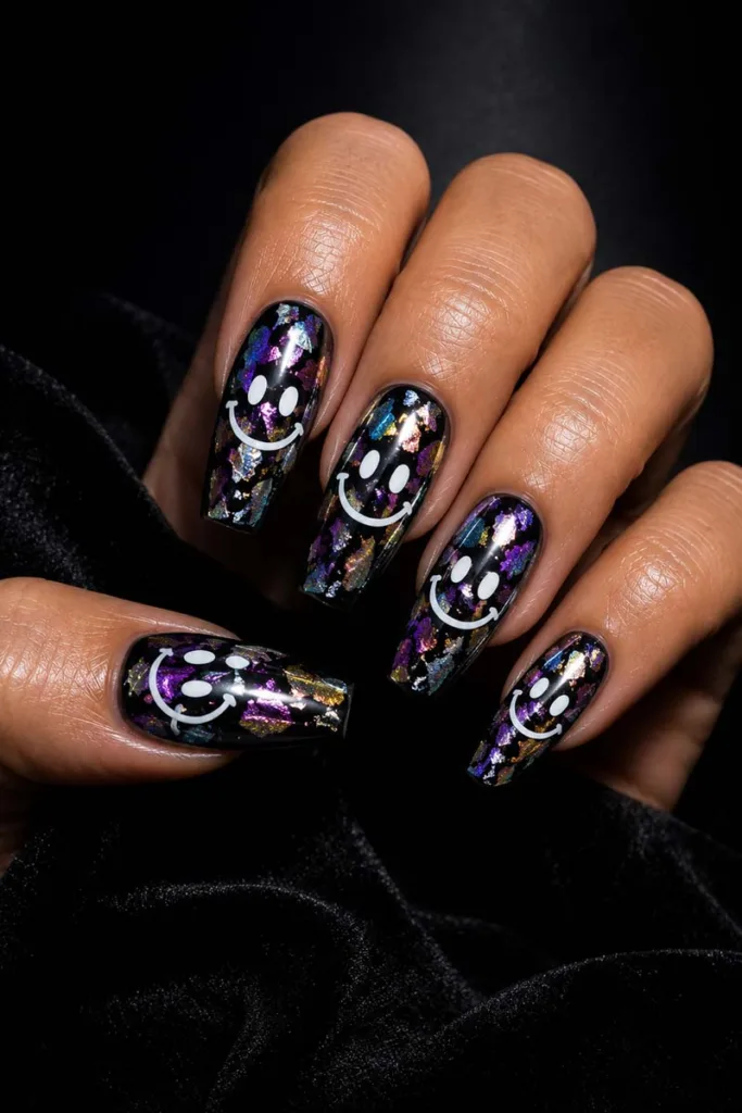 Close-up portrait of black coffin-shaped holographic smiley face nails with reflective foil nail art and glossy gel finish against a black velvet background under dramatic lighting.