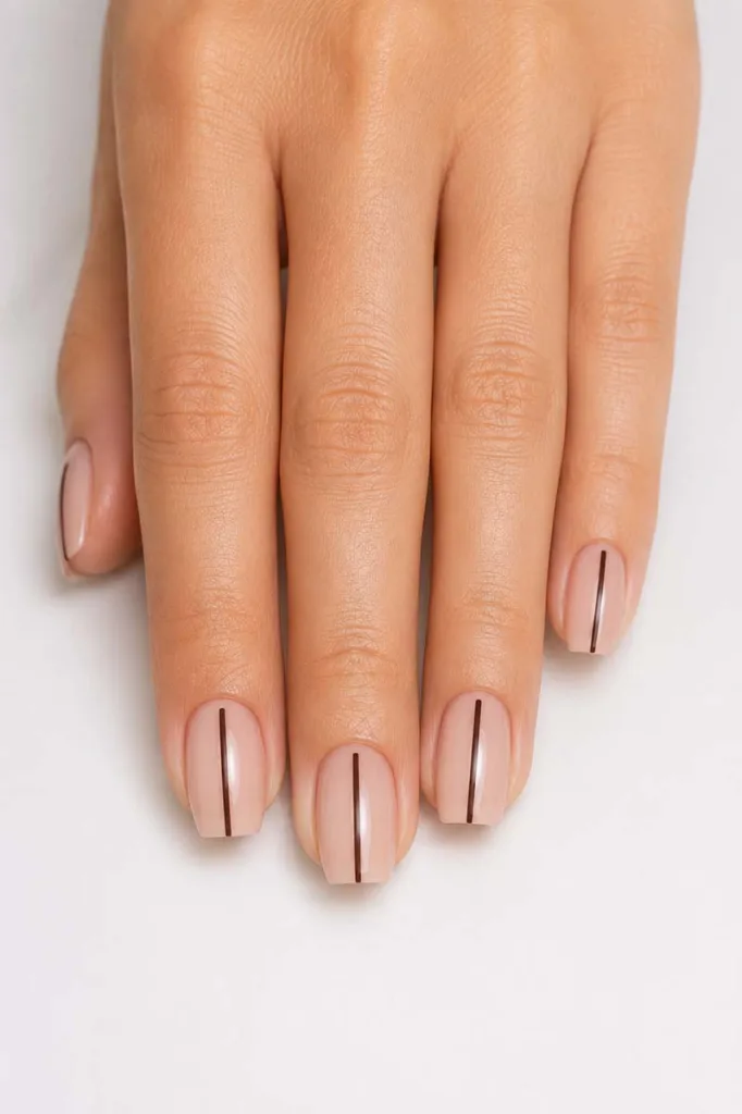 Close-up portrait of a hand with short coffin nails featuring a single thin deep brown vertical line centered on each sheer nude nail against a smooth white background with bright even lighting.