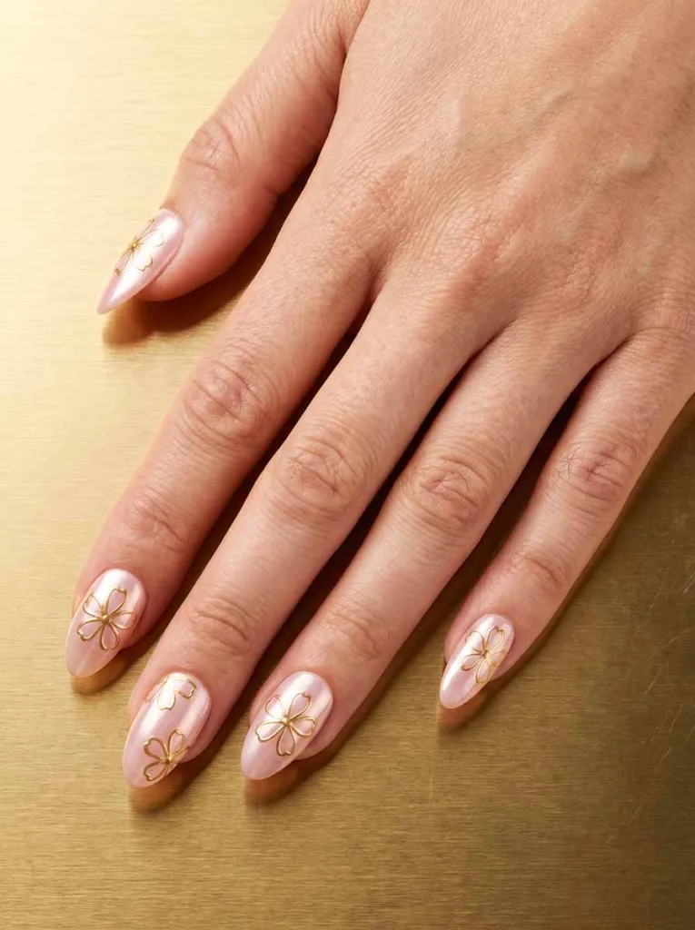 Almond-shaped pearl pink chrome powder nails with hand-drawn gold gel pen five-petal blossom outlines on each nail