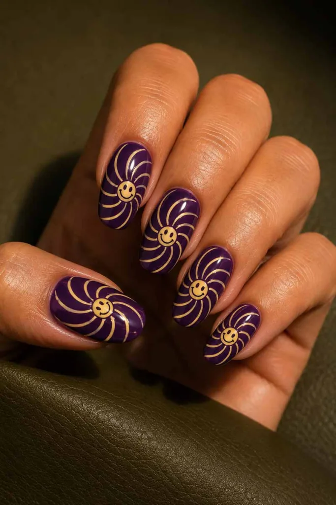 Close-up portrait of deep purple oval-shaped smiley face nails with cream spiral swirl nail art and glossy finish resting on a dark olive green surface under warm side lighting.