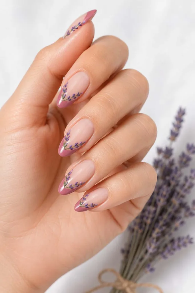 Almond-shaped nude nails with a rose pink V-shaped French tip and delicate lavender sprig floral detailing along the tip line