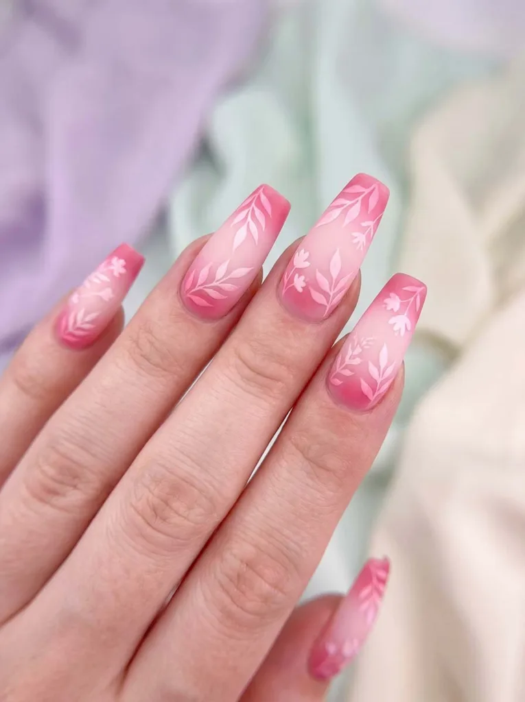 Coffin-shaped pink aura gradient nails with airbrushed botanical flower silhouettes in white and pale pink over a rose blush halo base