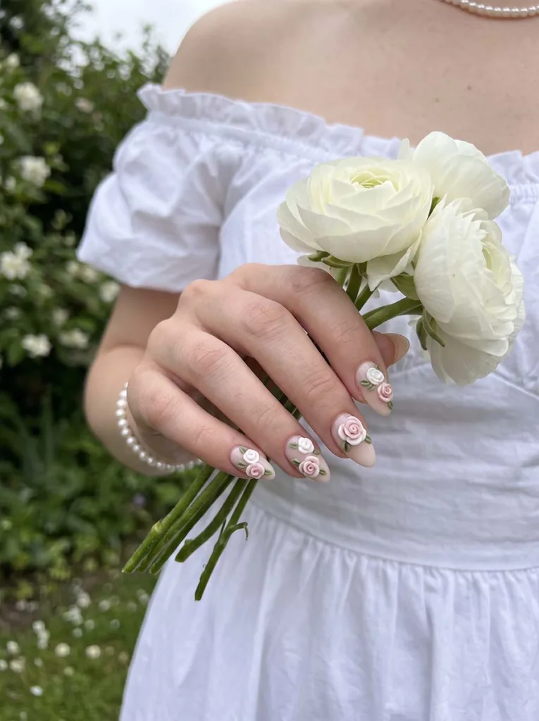 3D floral almond nail art with sculpted roses on fair skin hand near fresh flowers