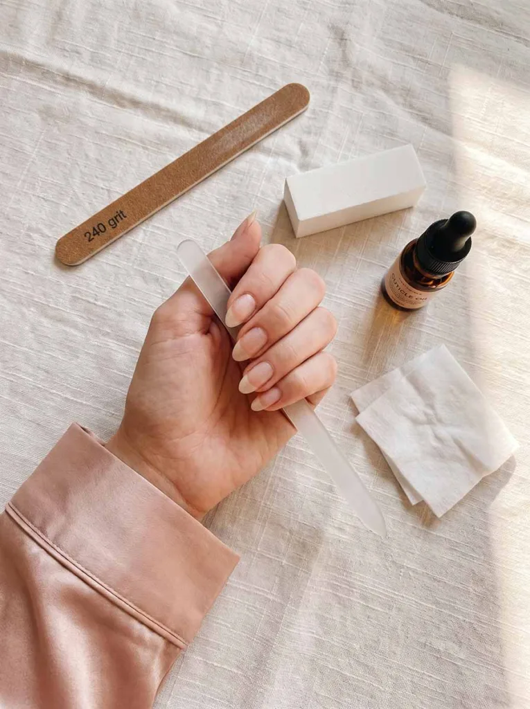 nail file tools laid flat for shaping almond nails at home including emery board buffing block and cuticle oil