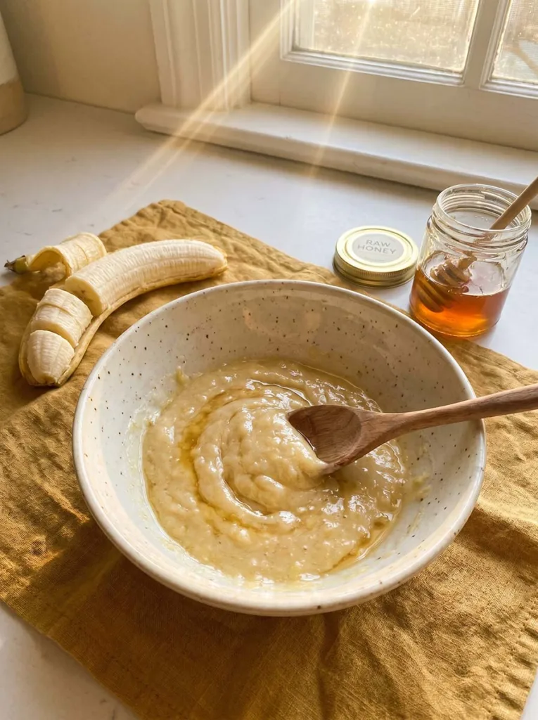 Banana and honey being mixed into a smooth yellow paste in a ceramic bowl for a DIY hair mask