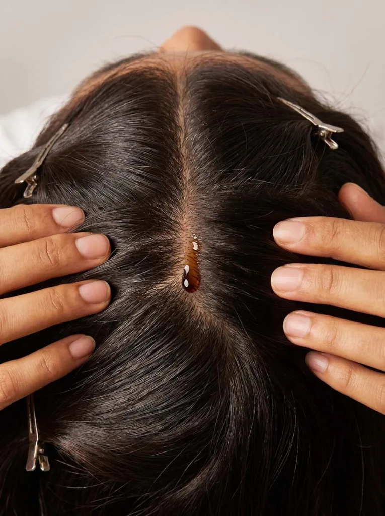 Overhead view of fingertips massaging castor oil into a parted scalp