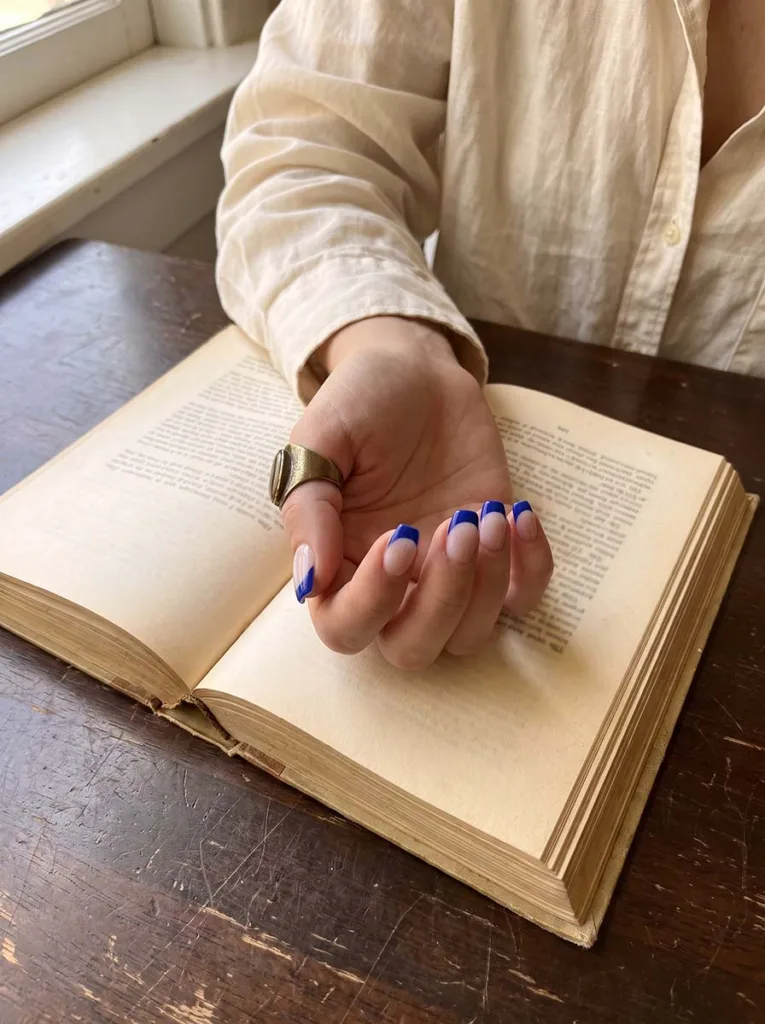 cobalt blue architectural French tip almond nails on fair skin hand holding open book