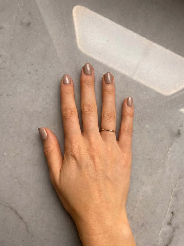 Creamy taupe short round nails on fair skin, overhead editorial shot on polished grey stone