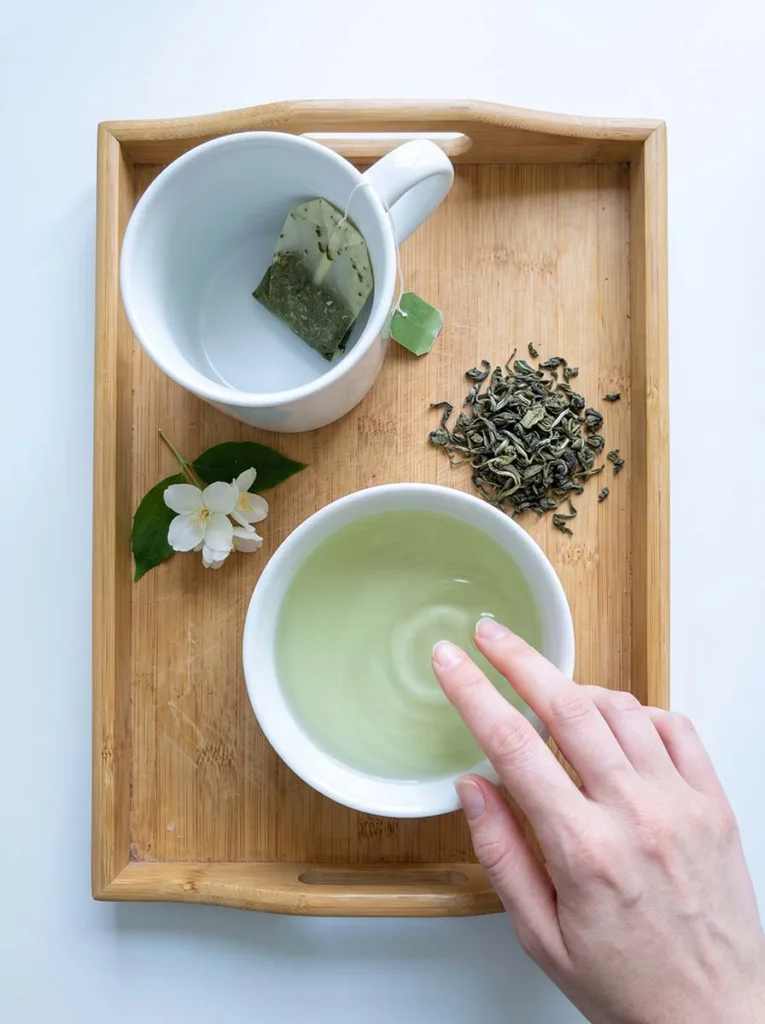woman soaking nails in a bowl of brewed green tea for antioxidant nail care at home