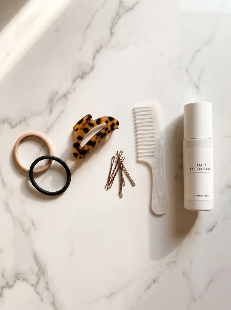essential hair tools flat lay including claw clip bobby pins hair ties and texturizing spray