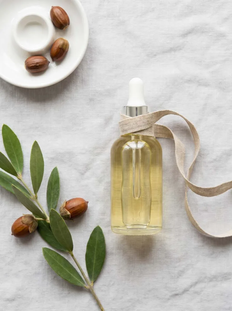pale golden jojoba oil in clear glass bottle on light grey linen in minimalist scandinavian flat lay