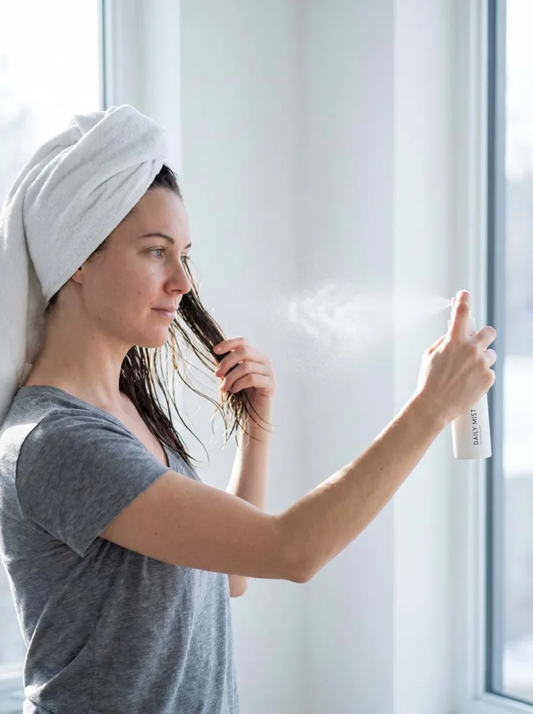 woman spraying leave-in conditioner onto damp hair after washing