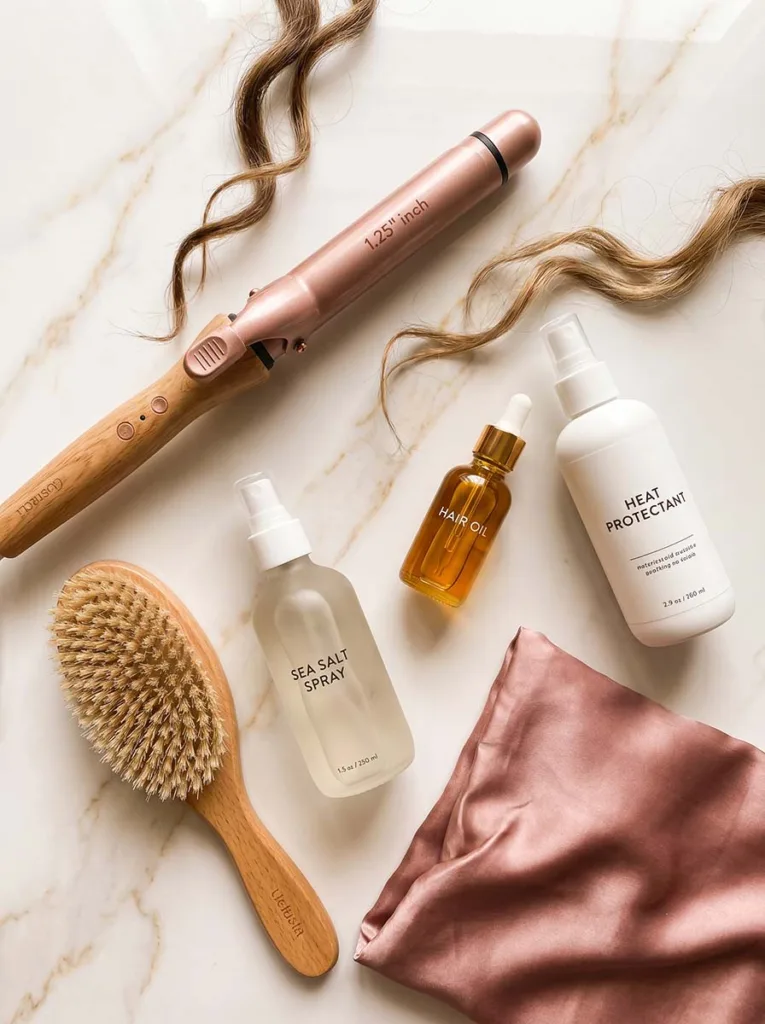 long hair styling tips — essential tools flatlay including curling iron, boar bristle brush, and sea salt spray