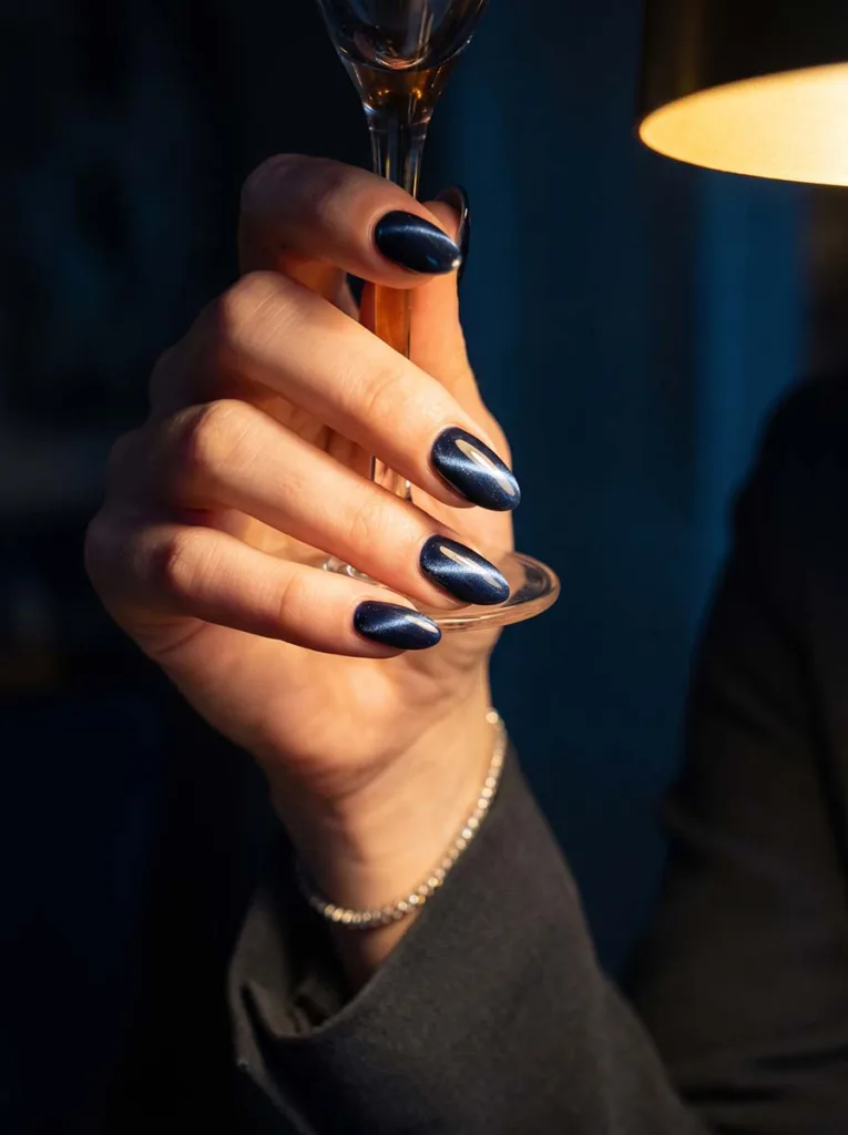 magnetic cat eye almond nails in midnight blue with metallic streak on fair skin evening look