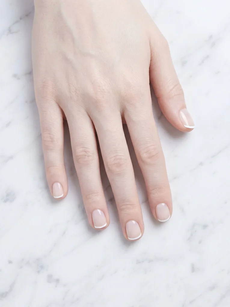 Micro French tip short round nails on very fair skin — overhead macro on white Carrara marble