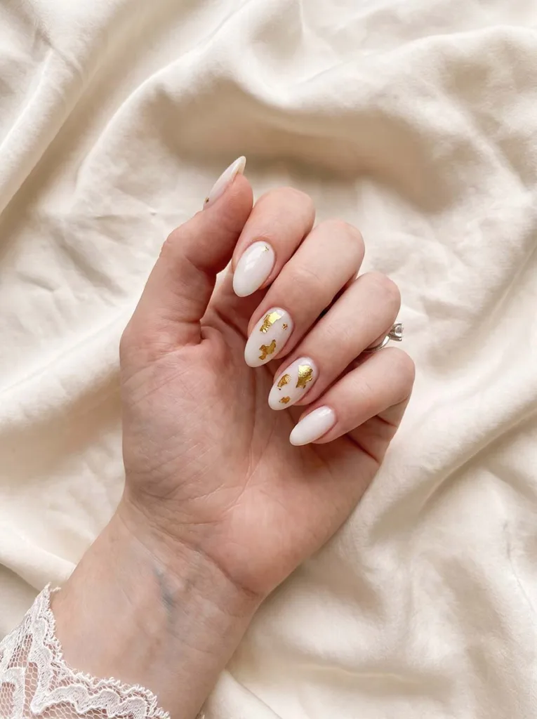 milky white almond nails with irregular gold foil flakes on fair skin bridal style close up