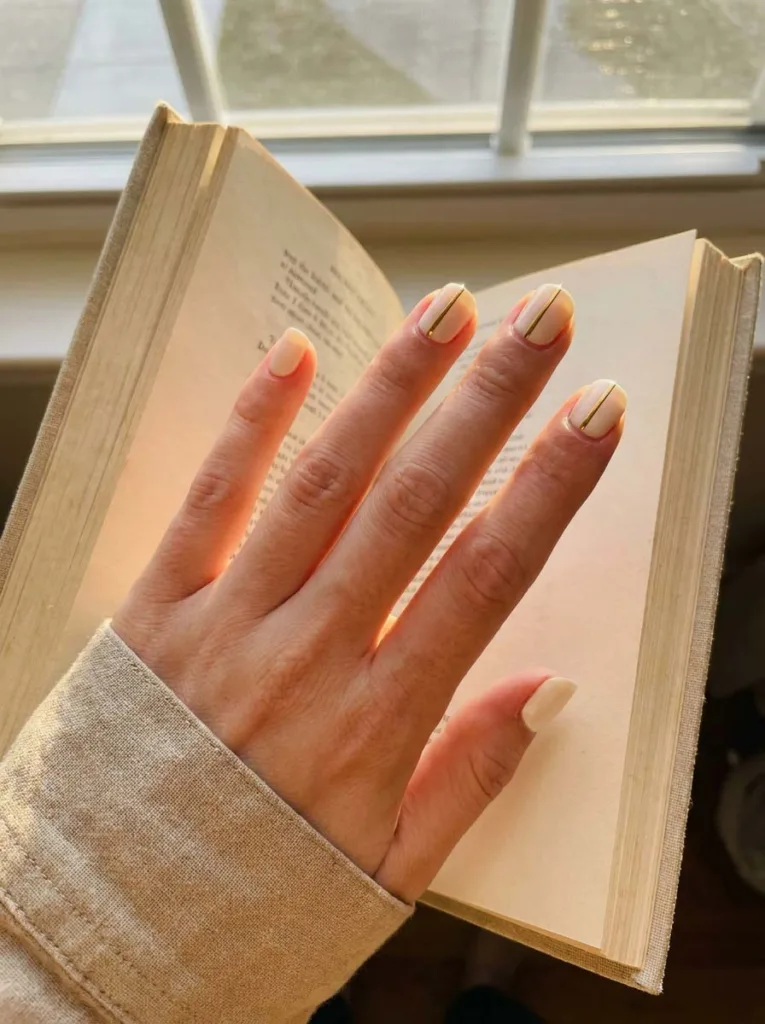 Minimalist thin gold vertical line nail art on short nails with pale nude base on fair skin