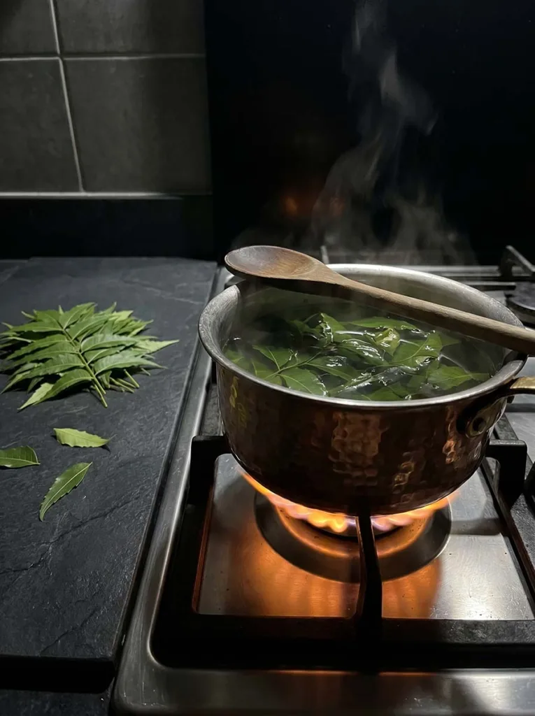 Fresh neem leaves boiling in water on a stovetop in a copper pot for a natural anti-dandruff scalp rinse