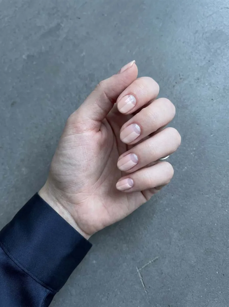 Negative space nail art on short oval nails with a clear half-moon at the cuticle and nude diagonal stripe