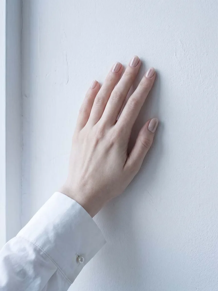 soft nude almond nails with thin minimalist center line on fair skin resting on white marble
