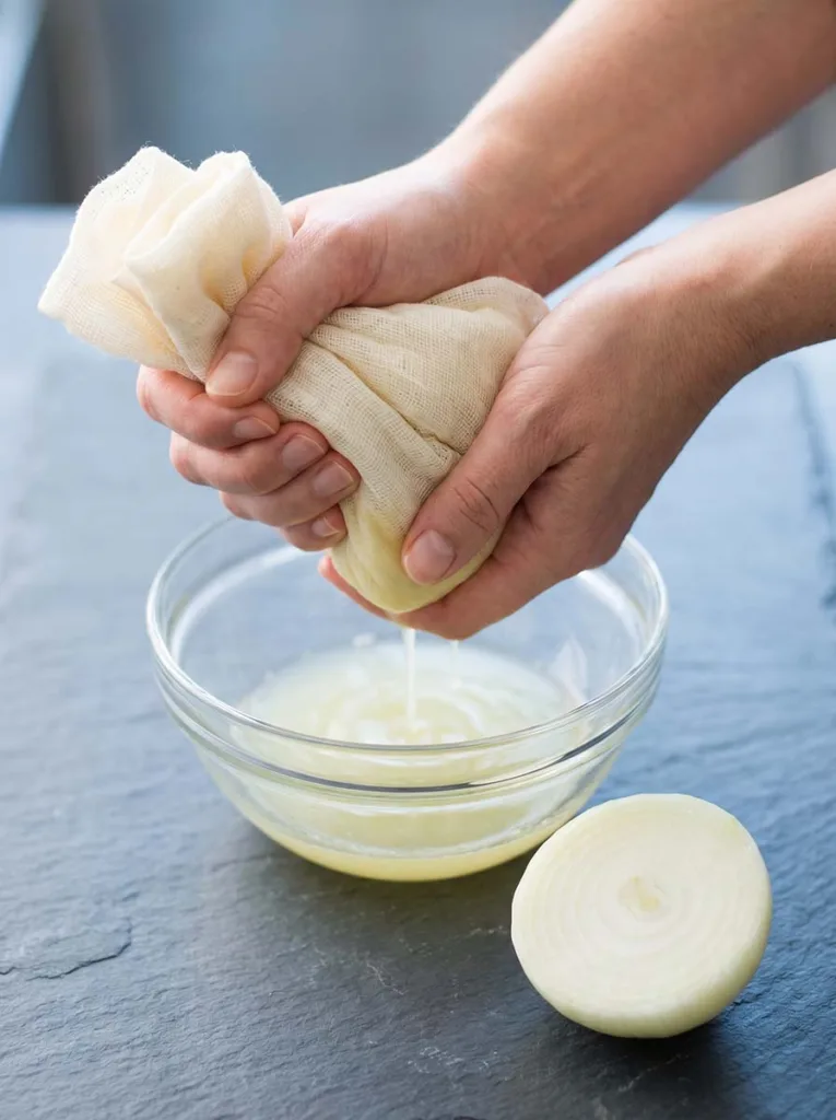 Close-up of hands squeezing fresh onion juice through cheesecloth into a small glass bowl