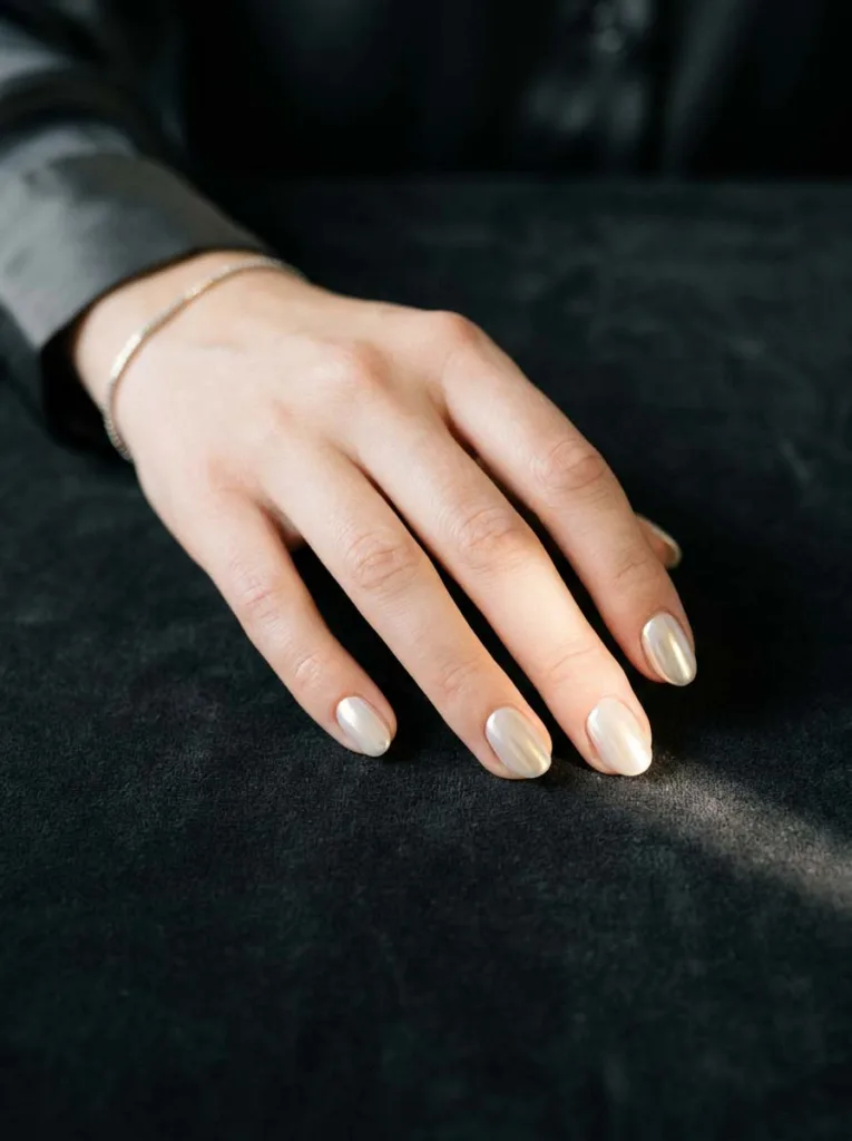 Pearl chrome metallic nail finish on short oval nails showing white to gold iridescent shift on fair skin