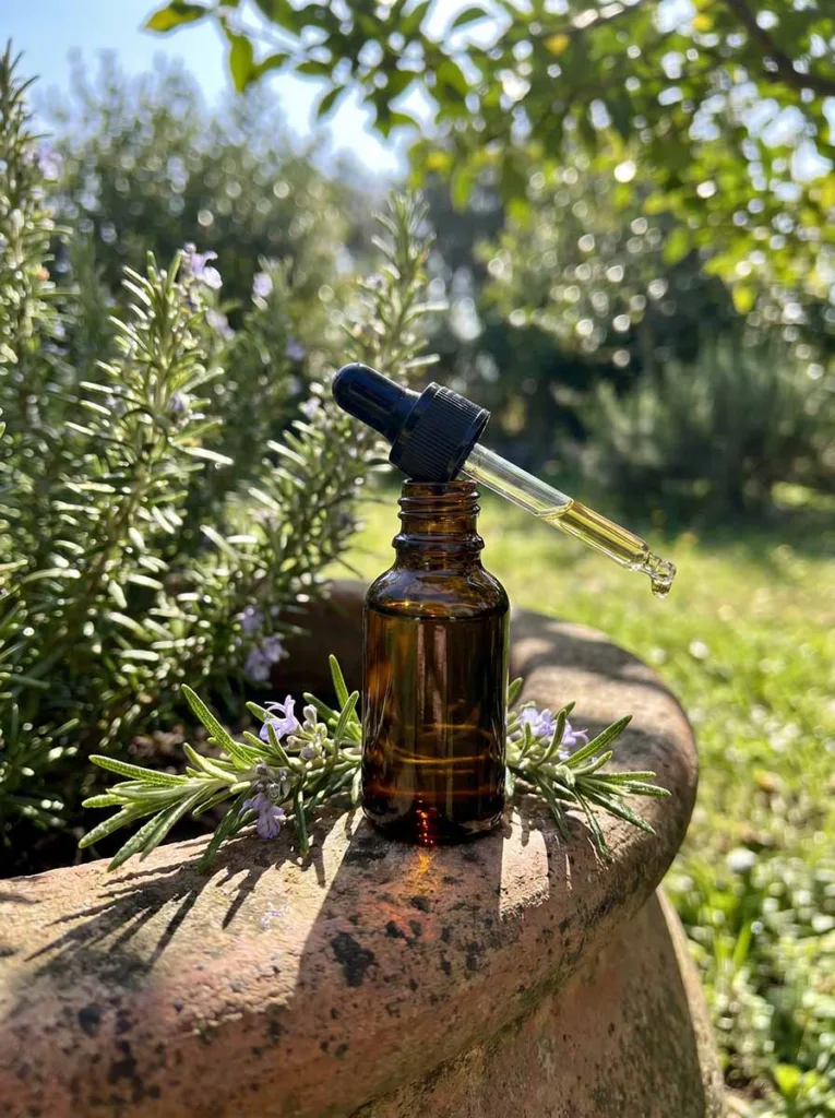 amber dropper bottle of rosemary essential oil surrounded by fresh rosemary in an outdoor garden setting