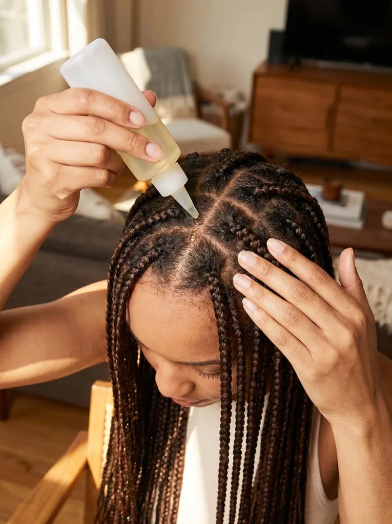 scalp care during protective styling — woman with box braids applying oil to scalp between parts