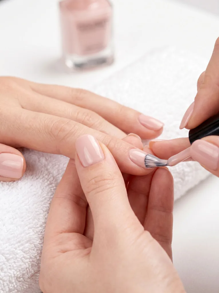 Professional nail polish application technique — brush sealing the tip of a short round nail, fair skin on white towel