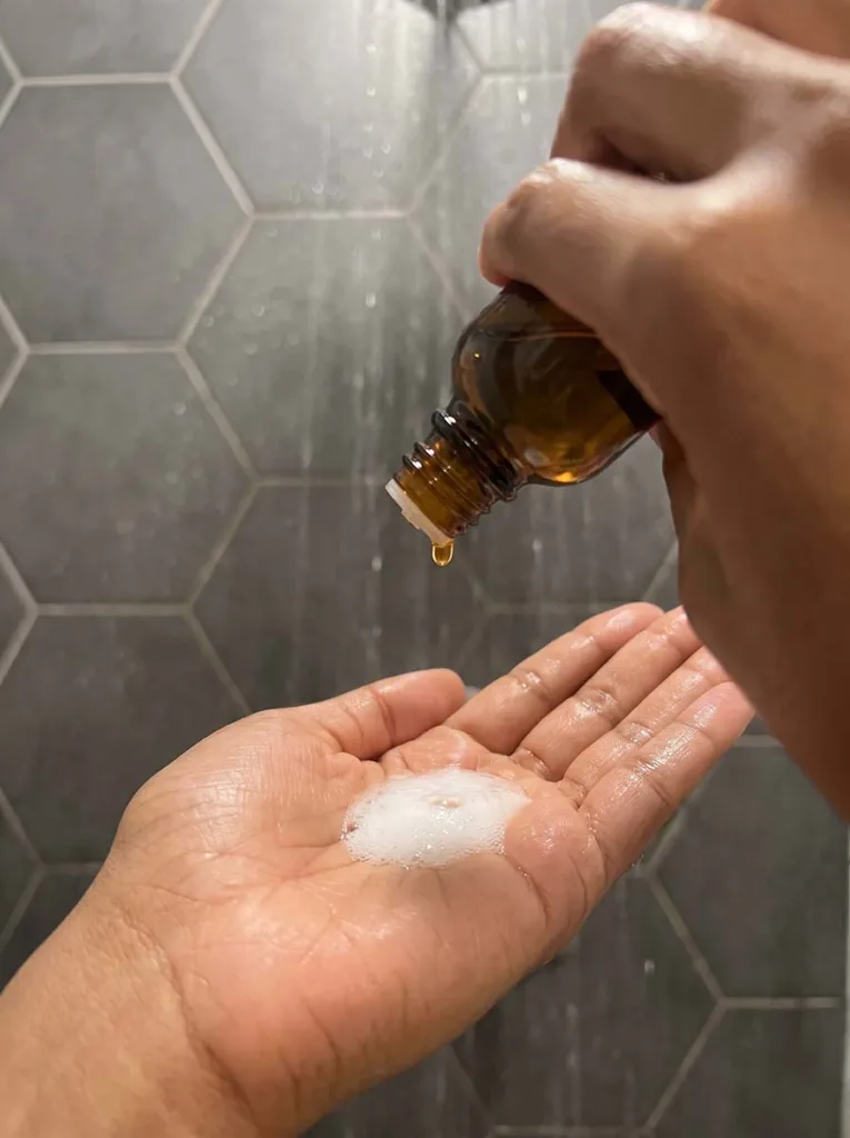 Five drops of tea tree oil being added to a palm full of shampoo lather for natural dandruff treatment