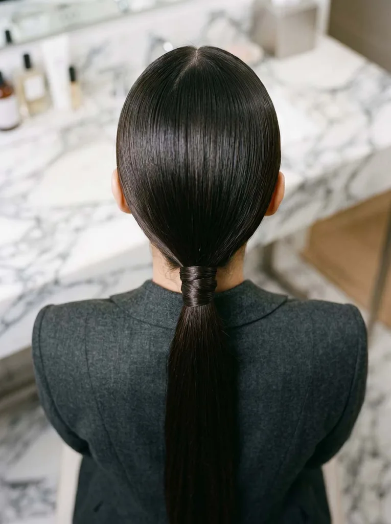woman with glossy dark hair in a low sleek ponytail photographed from directly behind at waist height looking down