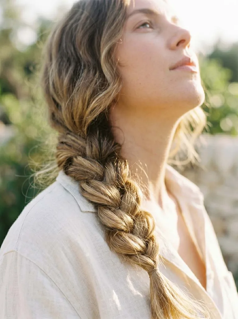 woman with long wavy hair in a loose side braid photographed from a low front angle looking up toward her collarbone