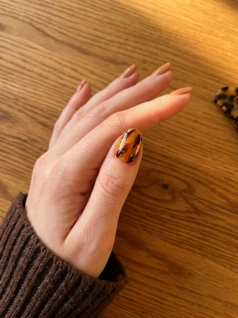Tortoiseshell accent nail art on one short nail with amber caramel and deep brown layered design, other nails plain nude