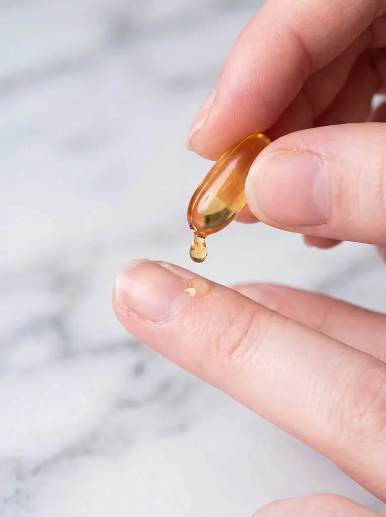 woman squeezing vitamin E oil from a capsule directly onto her nail cuticle for nail matrix regeneration