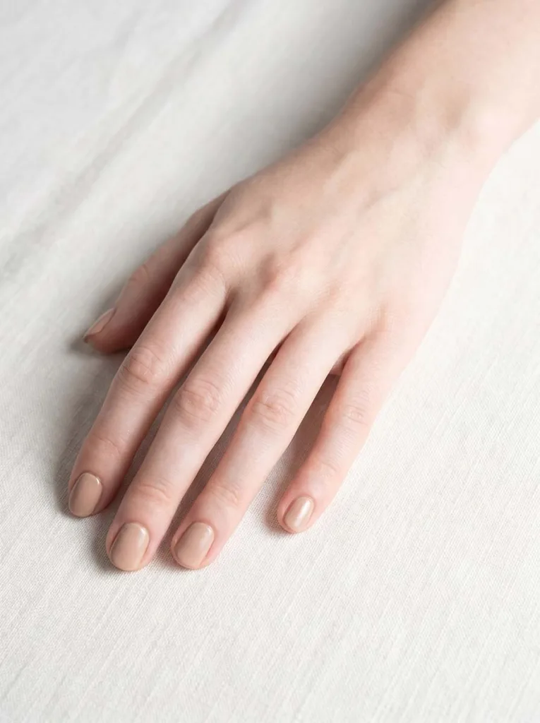 Warm beige short round nails on fair porcelain skin on ivory linen — clean editorial close-up
