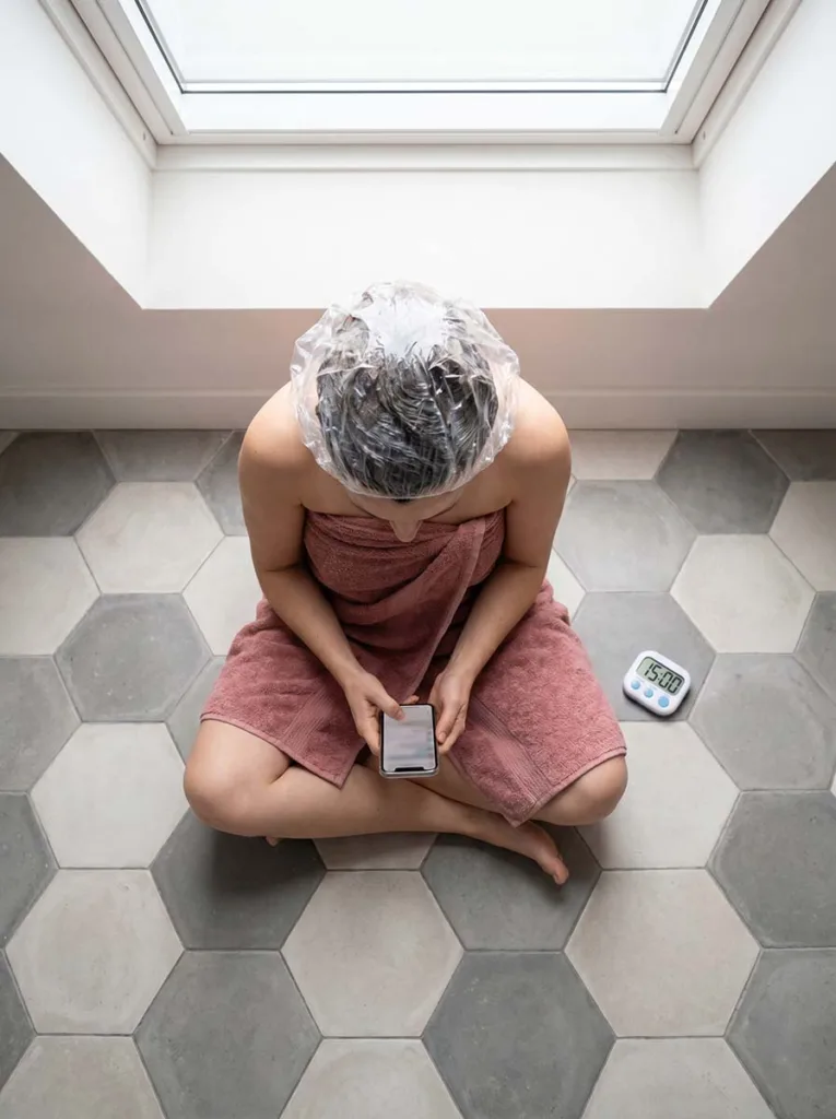woman sitting with deep conditioning hair mask and shower cap applied waiting for treatment to absorb