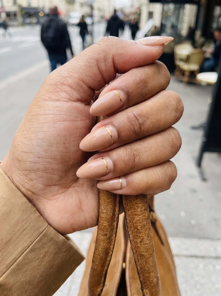 Almond-shaped peach nails with a gold accent line outdoors