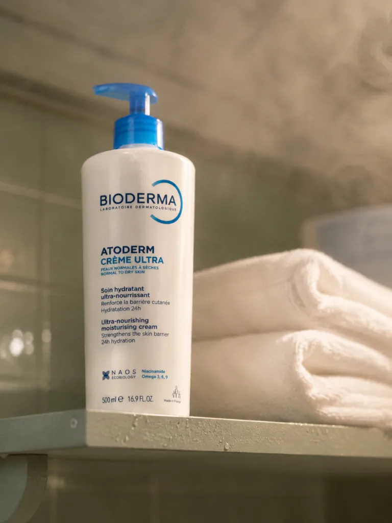 Bioderma Atoderm pump bottle on a bathroom shelf beside a folded towel stack