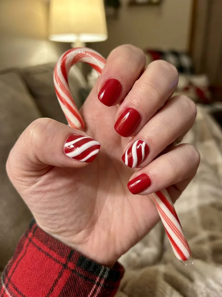 Candy cane stripe red christmas nails on a hand holding a candy cane