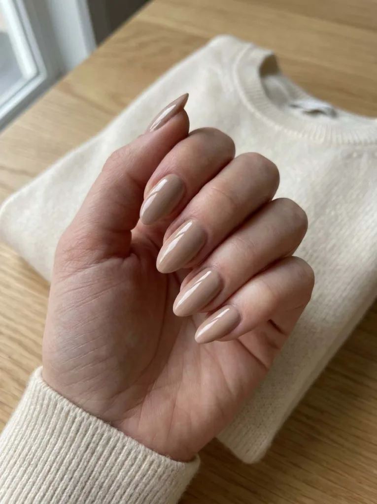 Cashmere beige glossy winter nails close-up on a cream sweater background