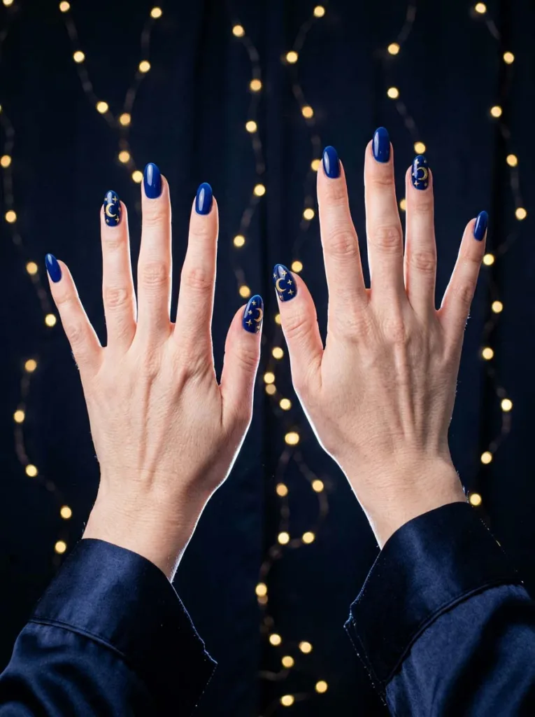 hand with celestial royal blue nail art reaching against a starry dark background