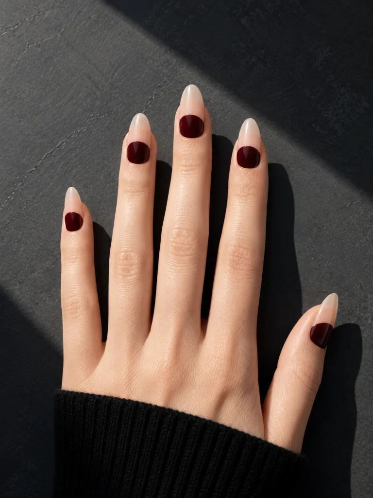 Reversed French nails with burgundy at the base and bare natural nail tips creating an architectural line on dark charcoal slate