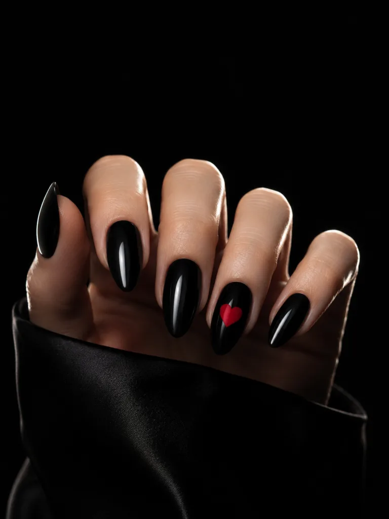 Black gel almond nails with a single centered red heart on the ring finger shot at near-nail level against a matte black background with rim lighting