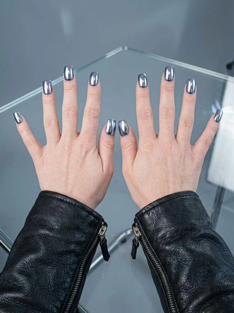 hand with chrome royal blue nails against a reflective glass surface
