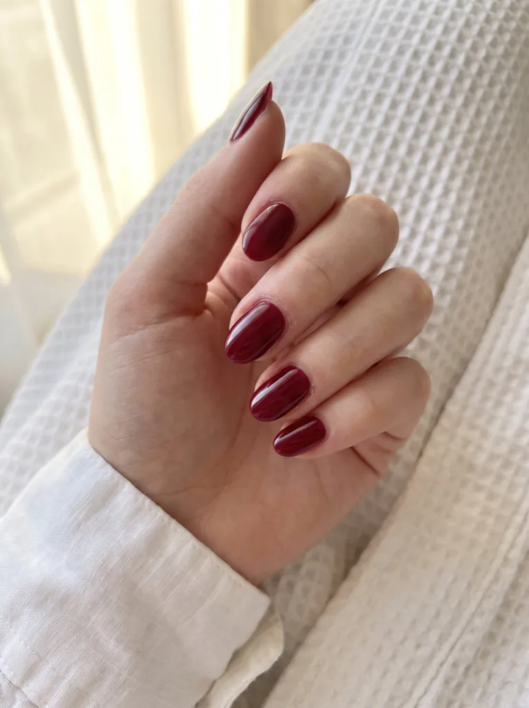 Close-up of classic cherry red nail polish on short almond nails with glossy finish resting on white waffle fabric